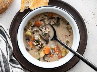 Overhead view of a bowl of Creamy vegetable wild rice soup with bread and a napkin on the side.