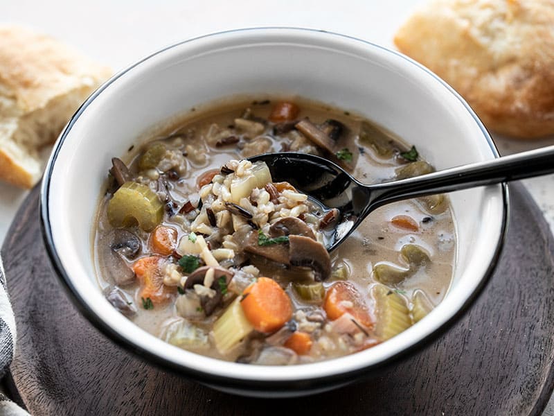 Front view of a bowl of creamy vegetable wild rice soup with a spoon lifting some out of the bowl