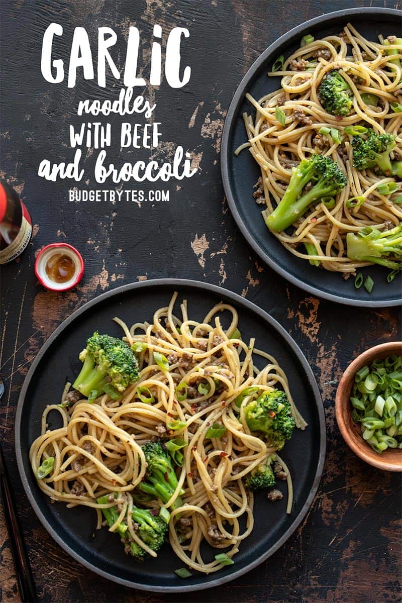 Two plates of Garlic Noodles with Beef and Broccoli next to a bowl of green onions and a bottle of oyster sauce