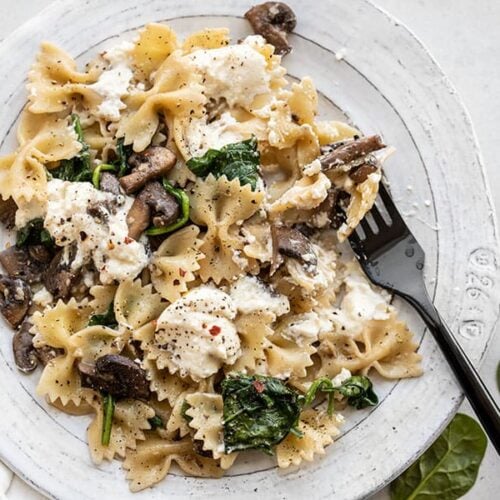 Close up of Mushroom and Spinach Pasta with Ricotta on a plate with a black fork.