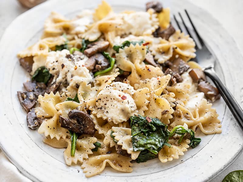 Close up side view of Mushroom and Spinach Pasta with Ricotta on a plate with a black fork.