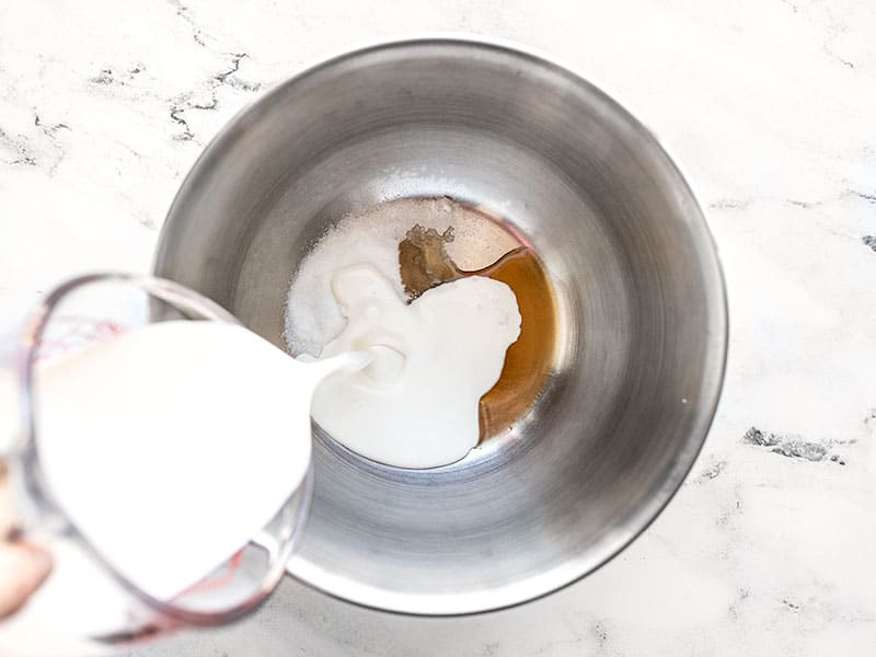 Heavy cream being poured into a bowl with sugar and vanilla