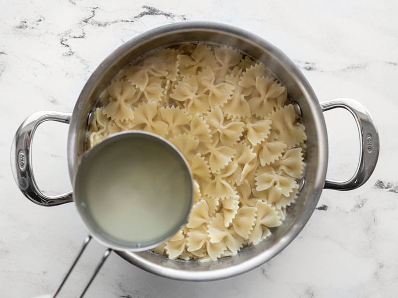 Cooked bowtie pasta with starchy pasta water in a measuring cup on the side