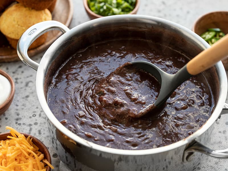 Side view of Smoky Black Bean Soup in the pot with a ladle lifting some, showing the thickness of the soup