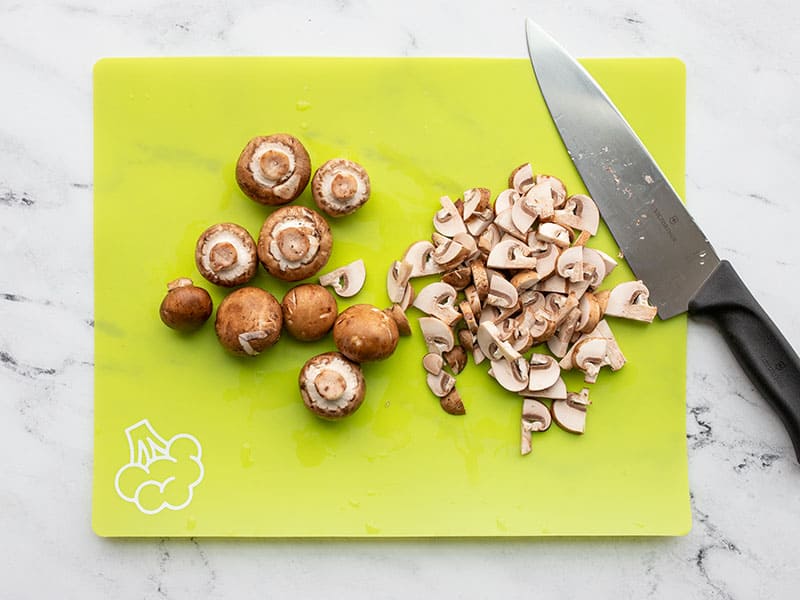 Mushrooms being sliced on a green cutting board