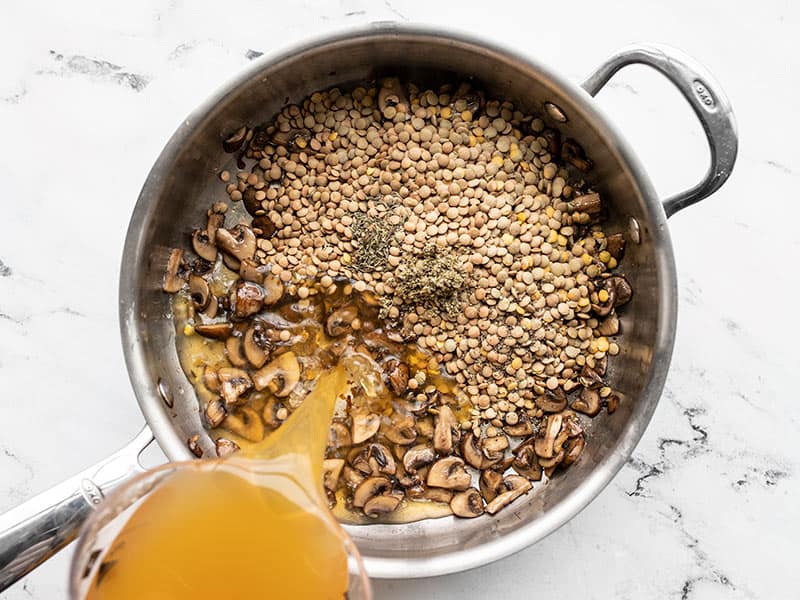 Lentils, herbs, and broth added to mushrooms in the skillet