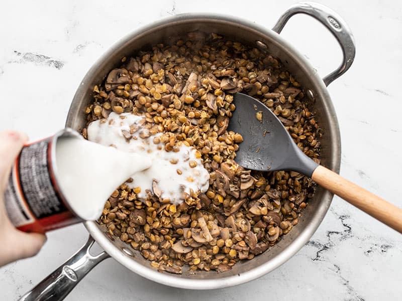 Coconut milk being poured into the skillet full of lentils