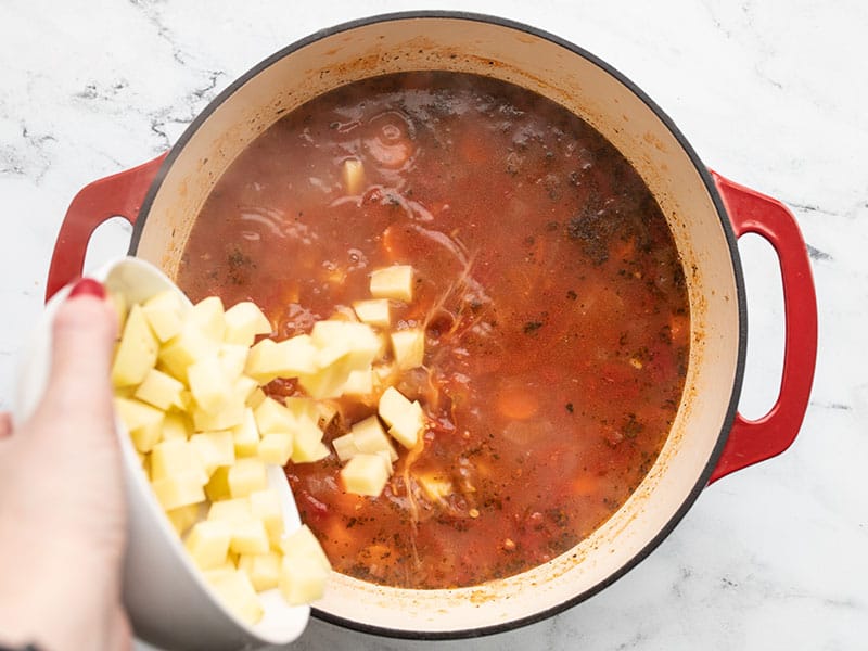 Diced potatoes being poured into soup