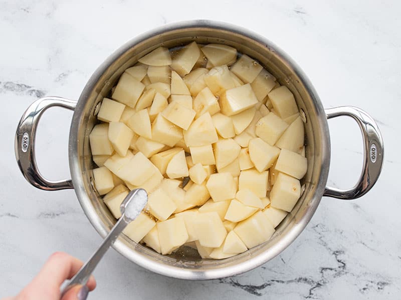 Mashed potatoes in a pot with water, salt being added