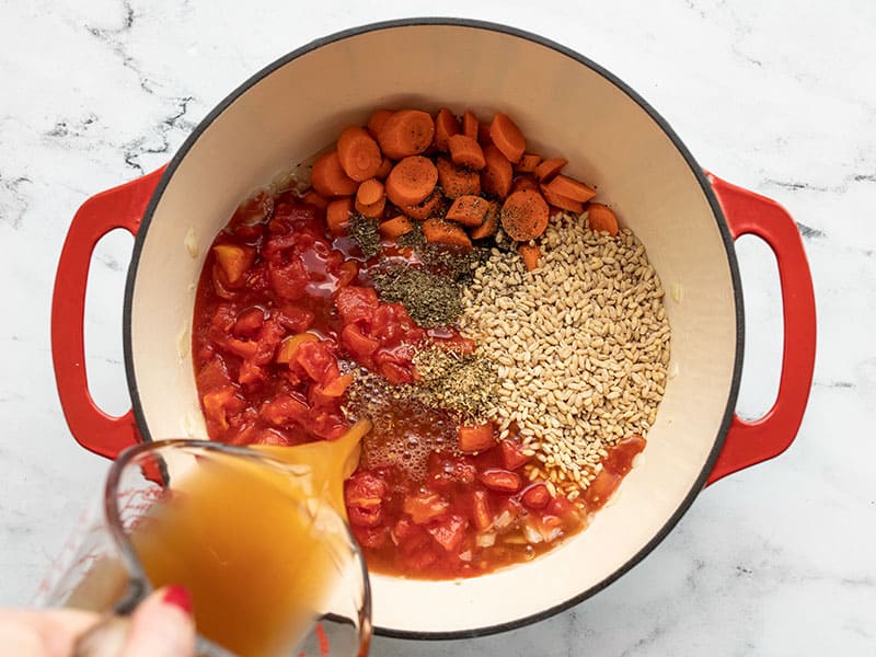 Broth being poured into soup pot with vegetables and barley