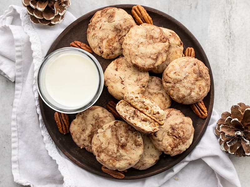 Overhead view of a plate full of Cinnamon Pecan Sandies with a glass of milk and one cookie broke in half.