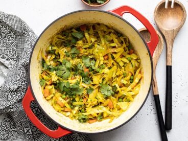 Curried Cabbage in a red pot with wooden utensils on the side.