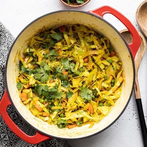 Curried Cabbage in a red pot with wooden utensils on the side.