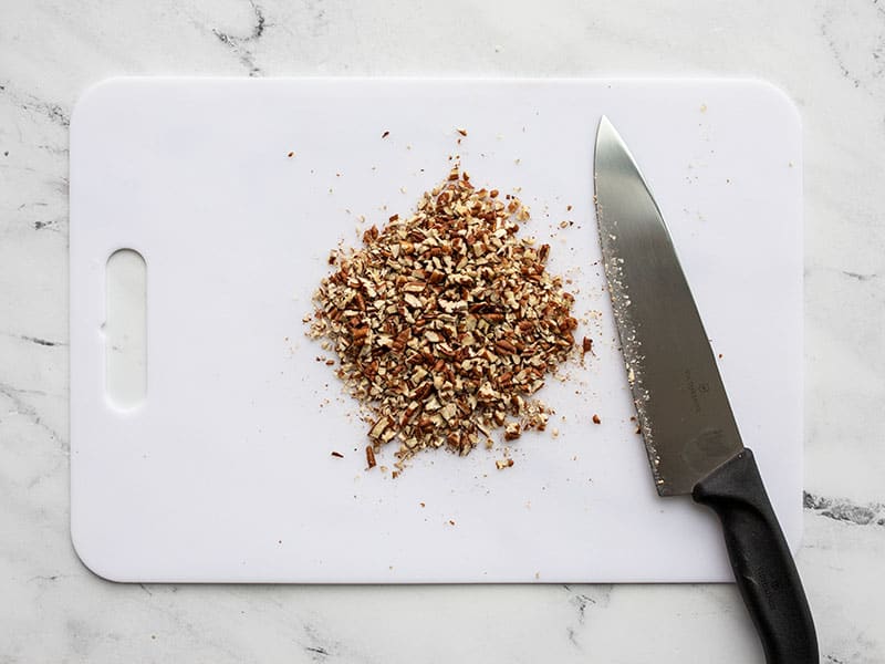 Finely chopped pecans on a cutting board with a knife.