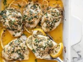 Overhead view of Garlic Butter Baked Chicken Thighs in the baking dish, one being scooped out with a serving spoon.