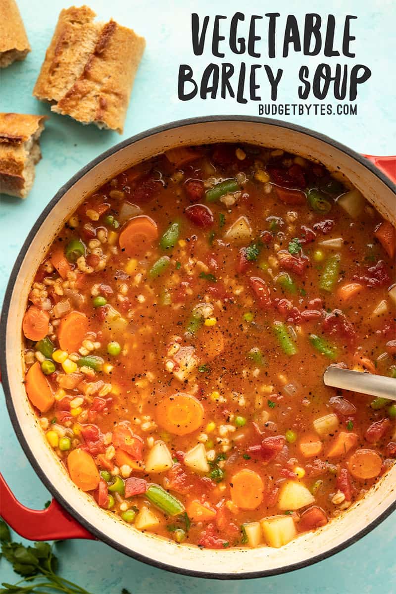 Overhead view of a pot full of Vegetable Barley Soup with bread and parsley on the side. Title text overlay at the top