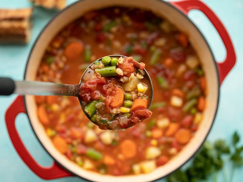 Close up of a ladle full of Vegetable Barley Soup being held over the soup pot.