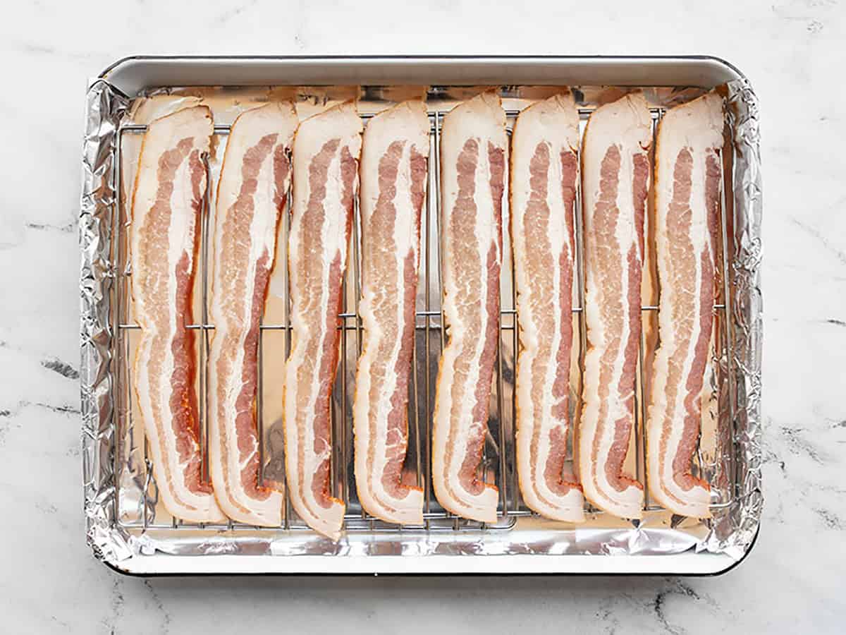 Raw bacon strips lined up on the prepared baking sheet. 