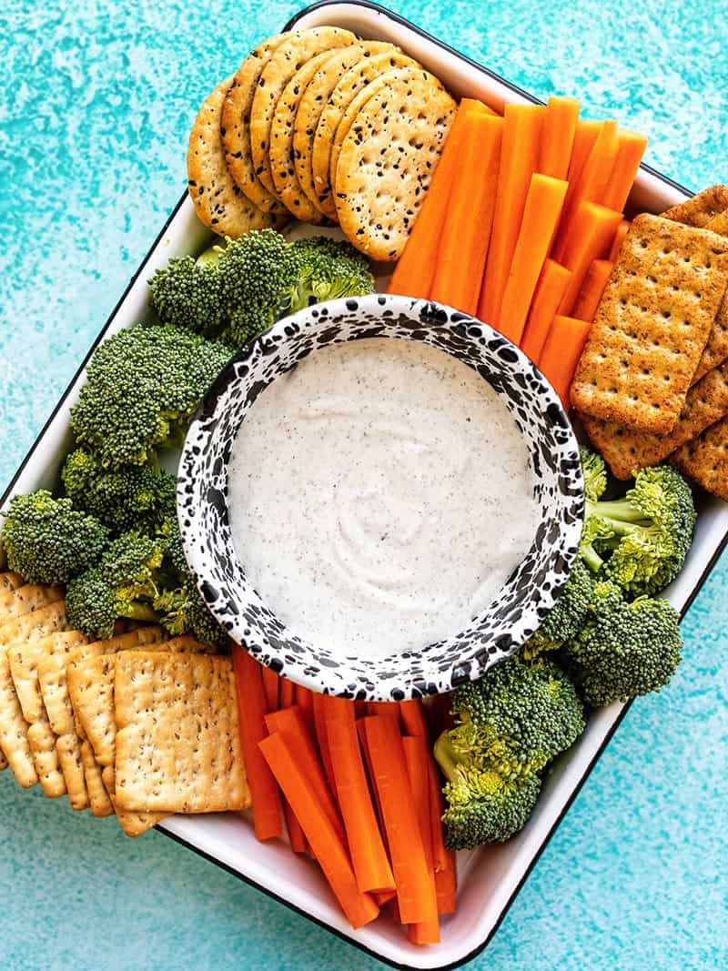 A platter full of crackers and vegetables with a bowl of garlic herb cottage cheese dip in the center