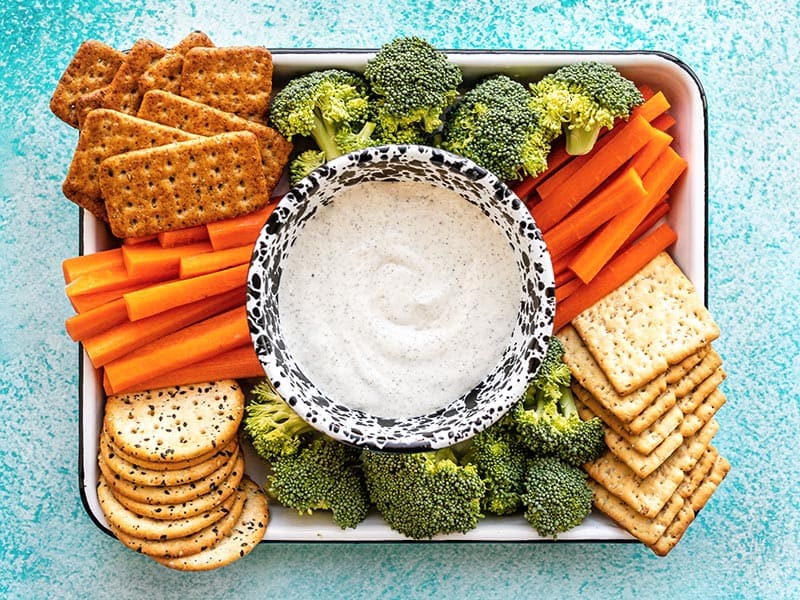 A platter full of crackers and vegetables with a bowl of Whipped Cottage Cheese Dip in the center