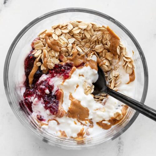 A spoon digging into a glass container full of a Peanut Butter and Jelly Cottage Cheese Breakfast Bowl