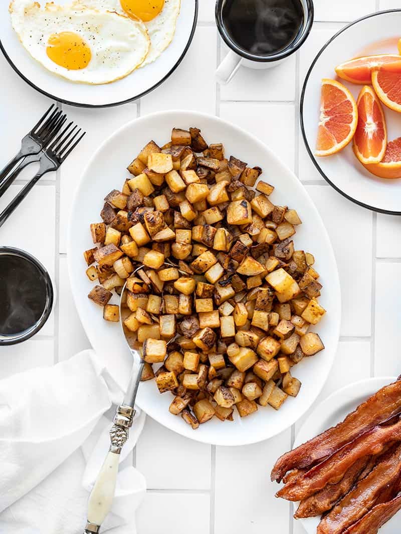 A serving platter full of Roasted Breakfast Potatoes with eggs, bacon, and oranges on the side