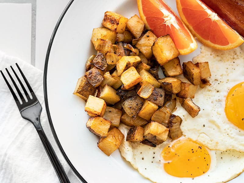 Close up of roasted breakfast potatoes on a plate with eggs and orange slices