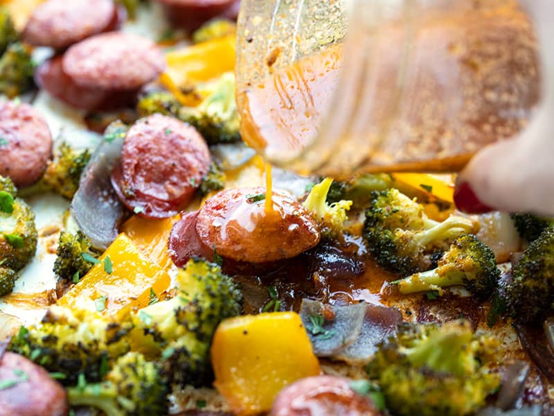 vinaigrette being drizzled over sausage and vegetables