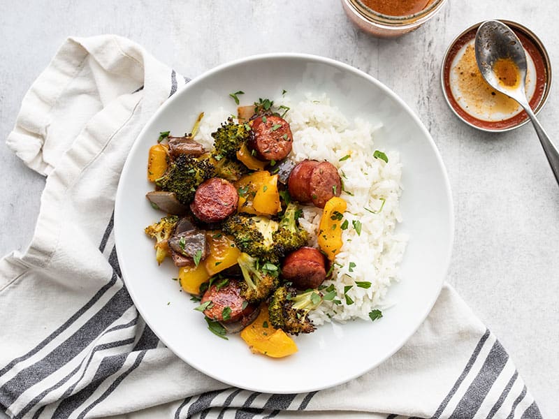 Overhead view of a plate with rice and roasted sausage and vegetables. Mason jar with vinaigrette on the side