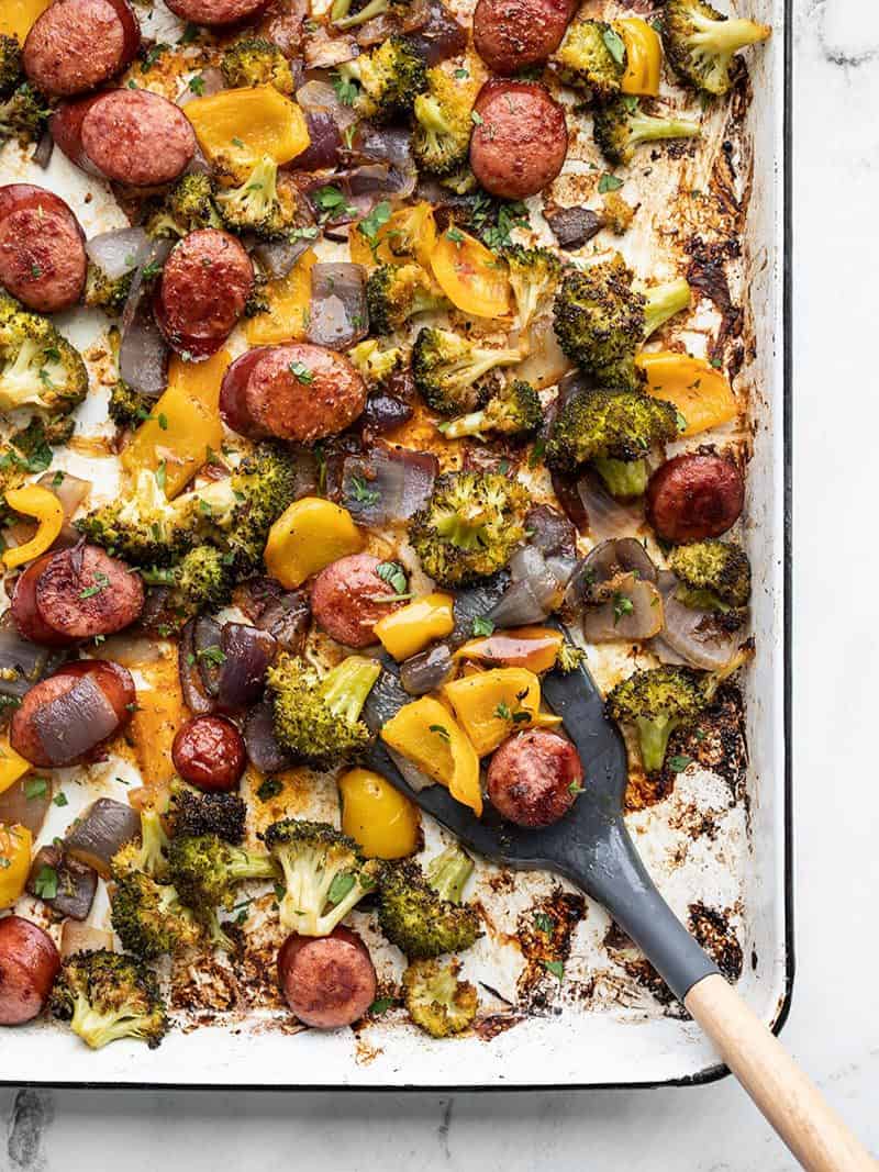 Smoky Roasted Sausage and Vegetables on the sheet pan with a spatula scooping some in the bottom corner