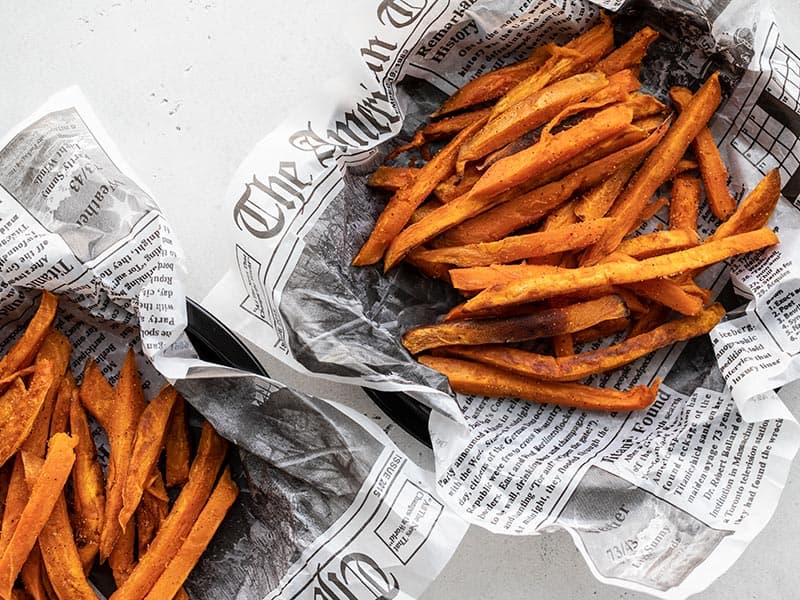 Overhead view of two dishes lined with newsprint containing spicy sweet potato fries