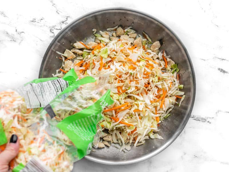 Coleslaw mix being poured into the skillet