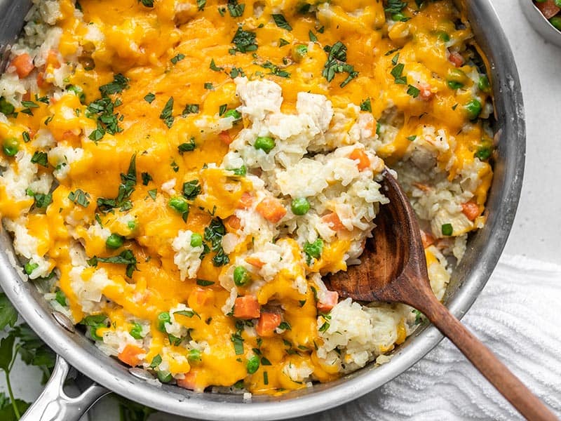 Close up of chicken and rice being scooped out of the skillet with a wooden spoon.