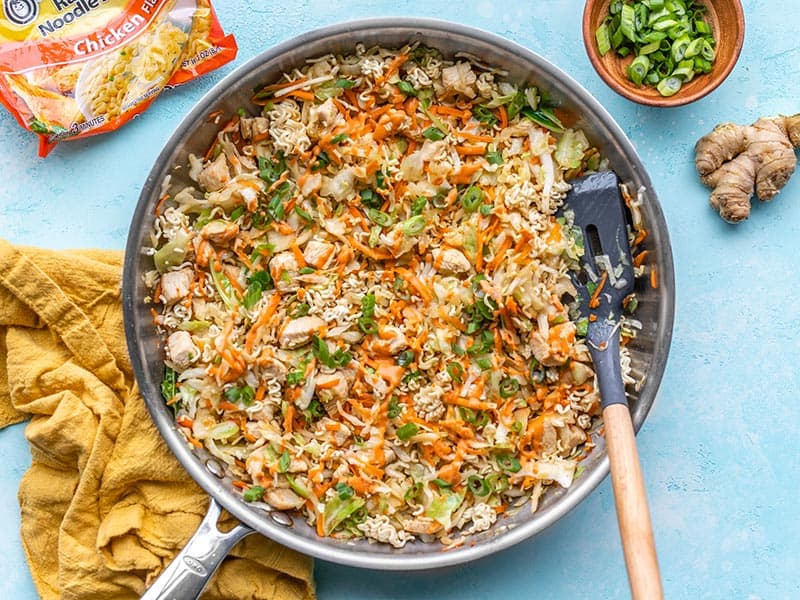 A skillet full of Crunchy Chicken Ramen Stir fry with a spatula in the side and a package of ramen on the left