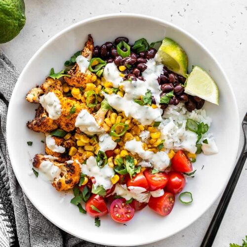 Overhead view of a roasted cauliflower taco bowl next to a lime and bowl of cilantro lime ranch