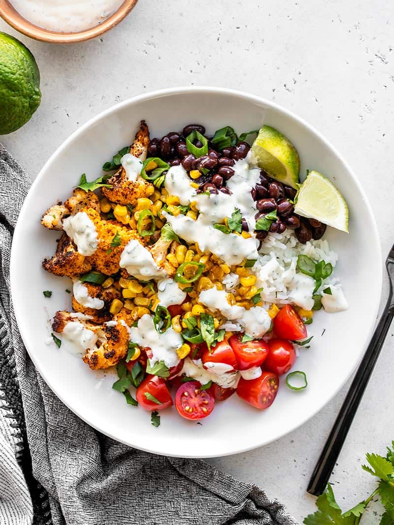 Overhead view of a roasted cauliflower taco bowl next to a lime and bowl of cilantro lime ranch