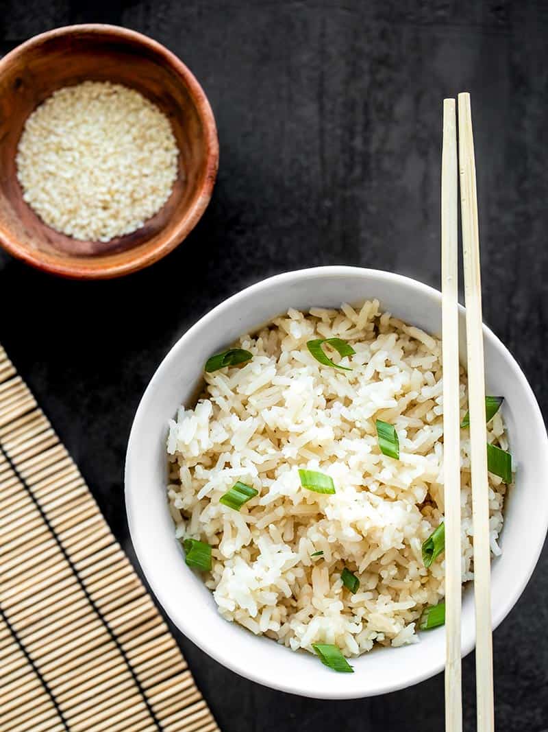 A bowl of sesame rice with chopsticks balanced on the rim and a small bowl of sesame seeds on the side