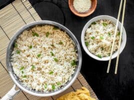 A pot full of sesame rice with a bowl of sesame rice on the side, both garnished with green onion