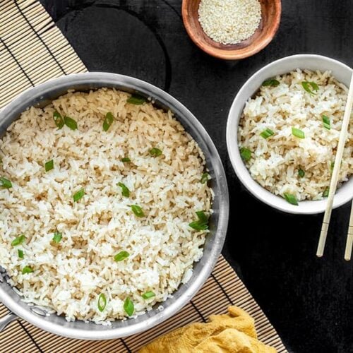 A pot full of sesame rice with a bowl of sesame rice on the side, both garnished with green onion