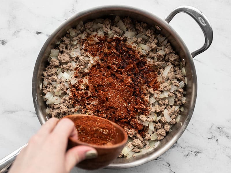 Taco seasoning being added to the skillet with turkey and onion