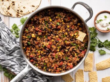 Overhead view of turkey taco skillet next to tortilla chips, a bowl of sour cream, and toasted tortillas