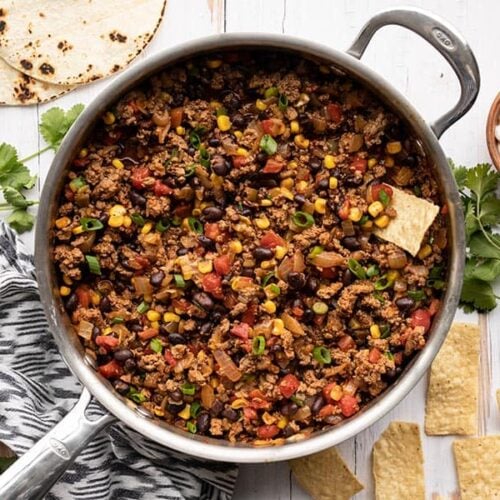 Overhead view of turkey taco skillet next to tortilla chips, a bowl of sour cream, and toasted tortillas