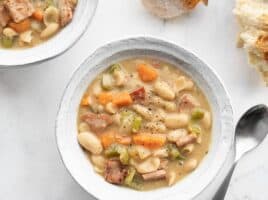 Two bowls of chunky ham and bean soup with chunks of bread on the side