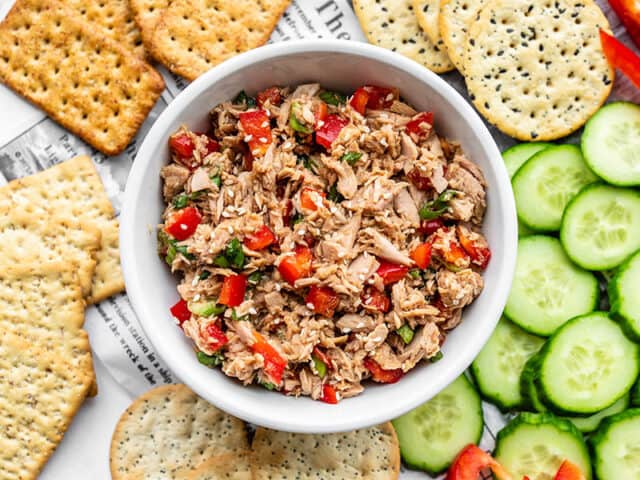 A bowl of sesame tuna surrounded by cucumber and crackers