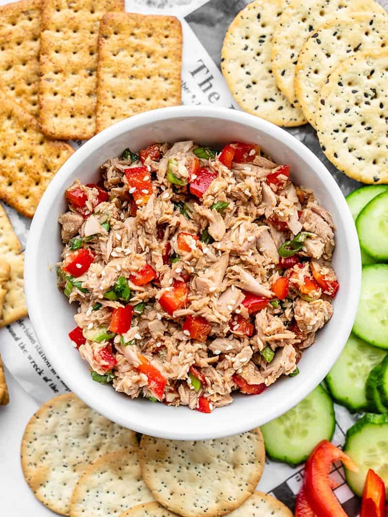 A bowl of Sesame Tuna Salad surrounded by crackers, cucumber slices, and red pepper slices