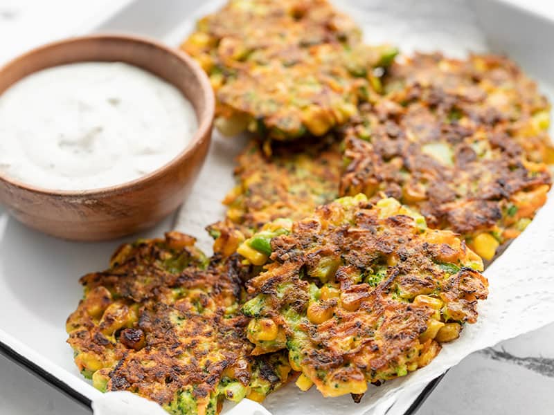 Front view of vegetable fritters on a tray with a small bowl of garlic herb sauce