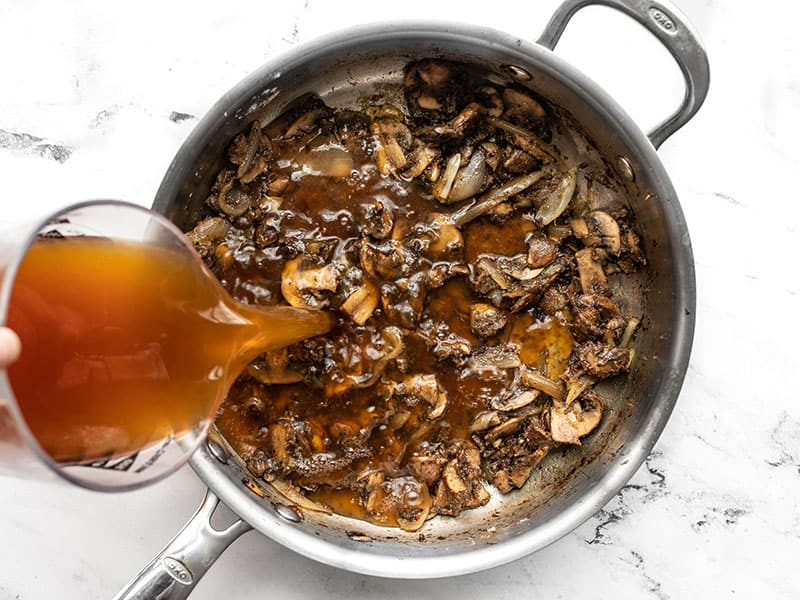 Beef broth being poured into the skillet