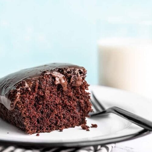 One slice of chocolate depression cake or "crazy cake" viewed from the side, a glass of milk in the background