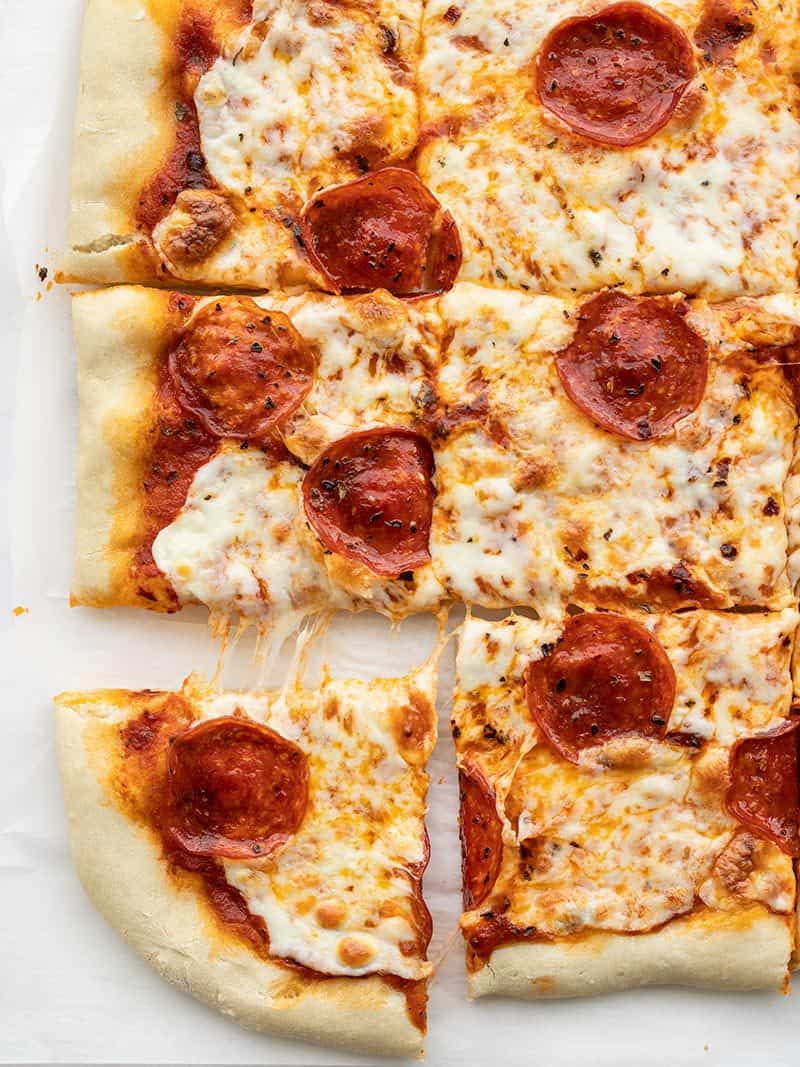 Overhead view of a rectangular pepperoni pizza with the corner piece being pulled out. 