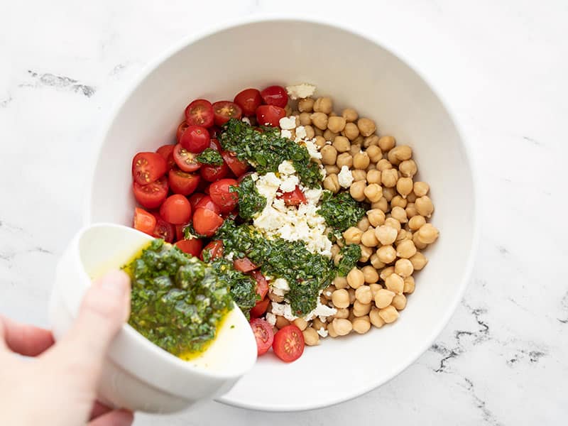 Chickpeas, tomatoes, and feta in a bowl, chimichurri being poured over top